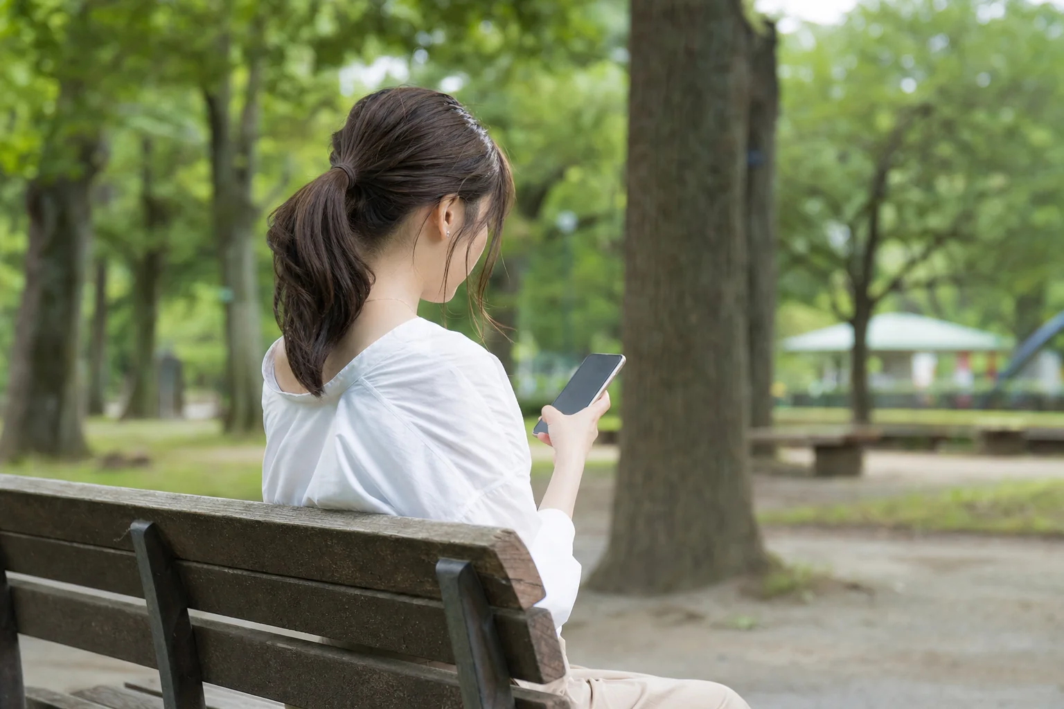 公園のベンチで一人でスマートフォンを見つめる女性の横顔